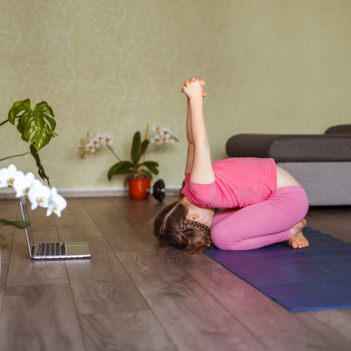 a little girl of six years doing yoga at home online with a laptop, children's health,the new normal