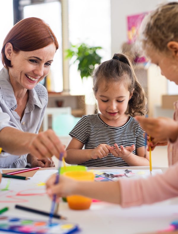 Group of small nursery school children with teacher indoors in classroom, painting